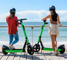 Two girls with electric scooters at the beach boardwalk