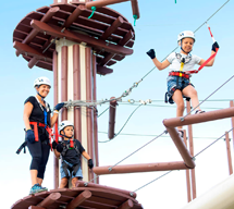 Mother and 2 small children climbing the ropes course in harnesses